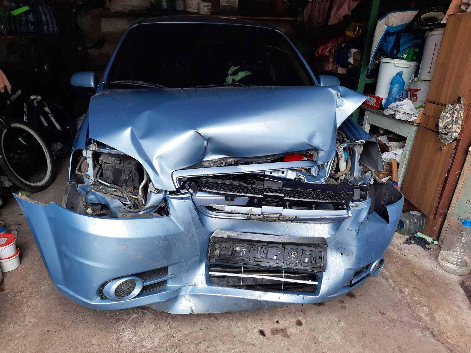 Разбитый синий автомобиль после ДТП с поврежденным передком в гараже